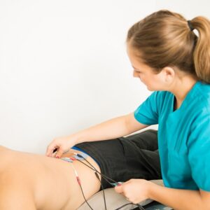 female physical therapist positioning electrodes customer lower back muscle treatment clinic