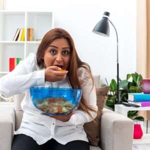 happy woman white shirt black pants relaxing sitting chair with bowl chips eating chips light living room